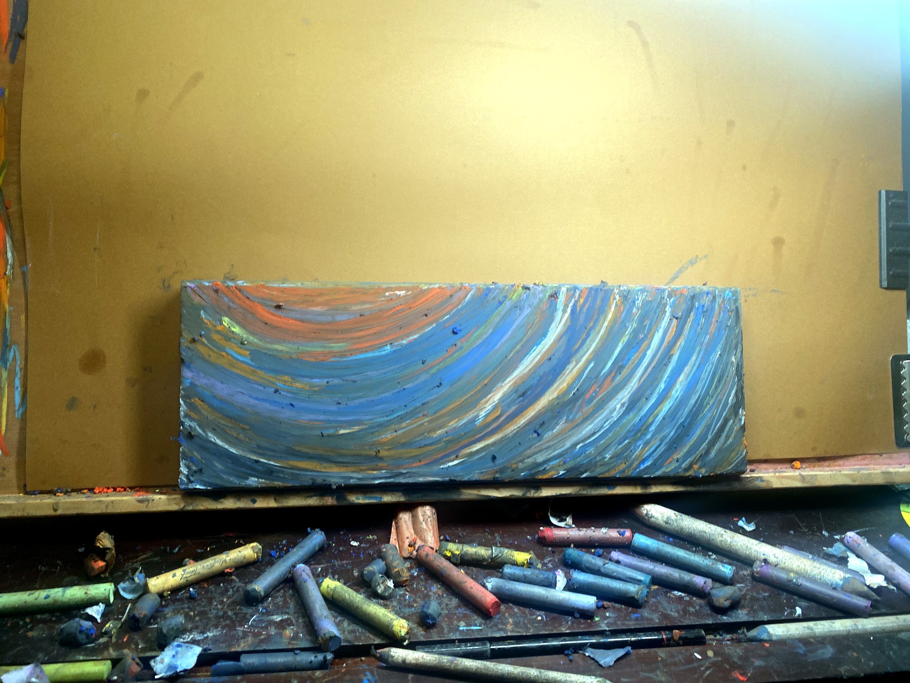 Rectangular painted wood panel with layered blue, gray, white, and warm curved marks in the studio.