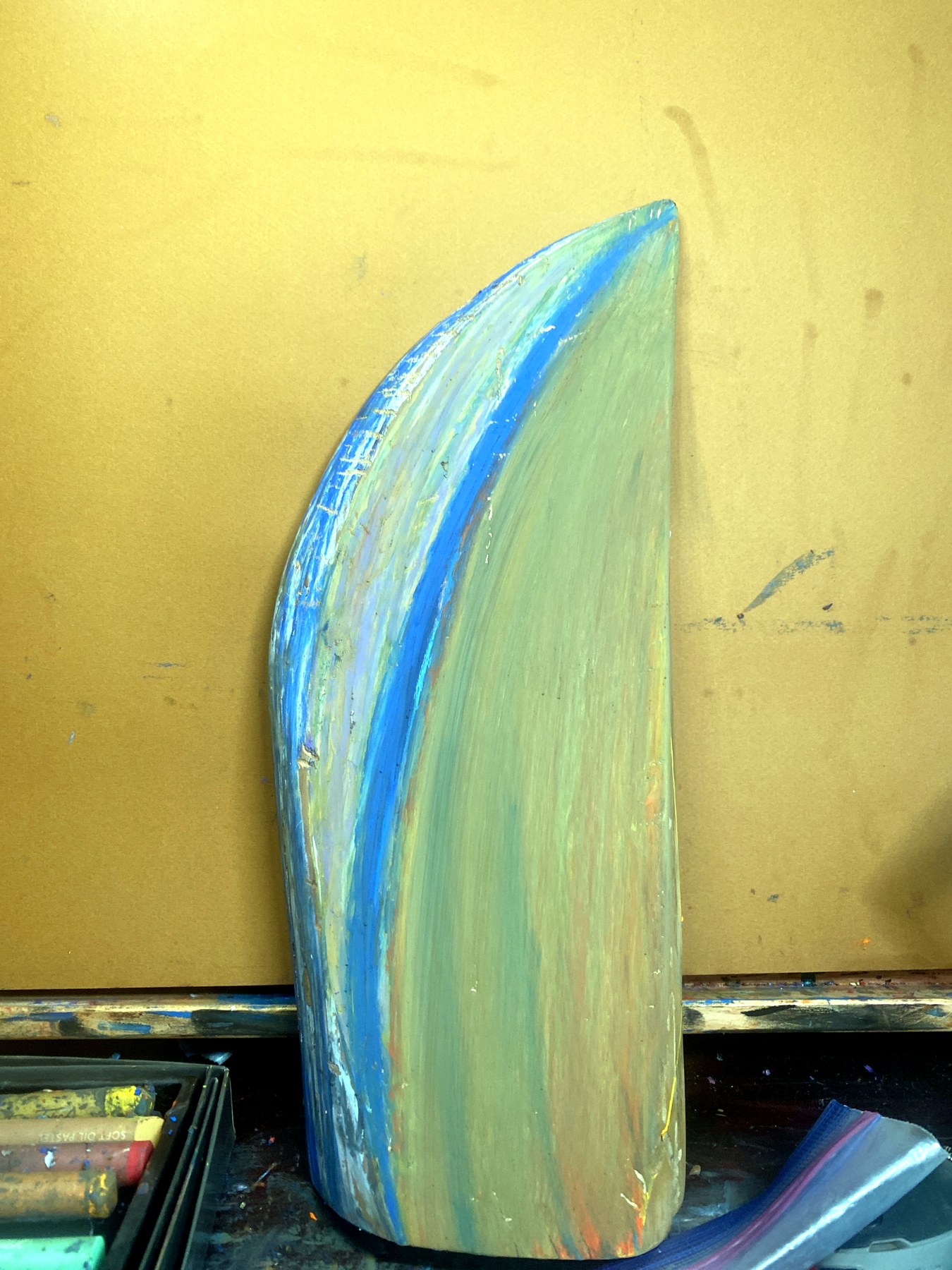 Tall curved painted wood object with pale green and blue bands, photographed upright in the studio.